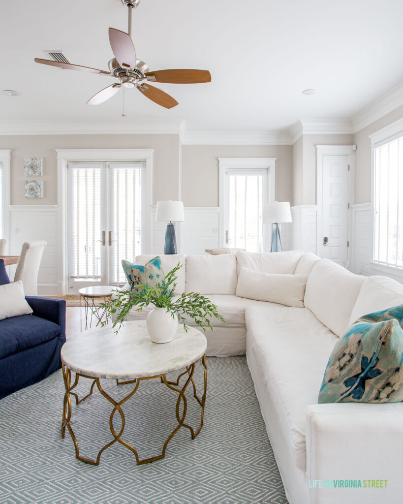 The Hola Beaches 30a living room including a white sectional, navy blue chairs, round coffee table, and colorful linen pillows.