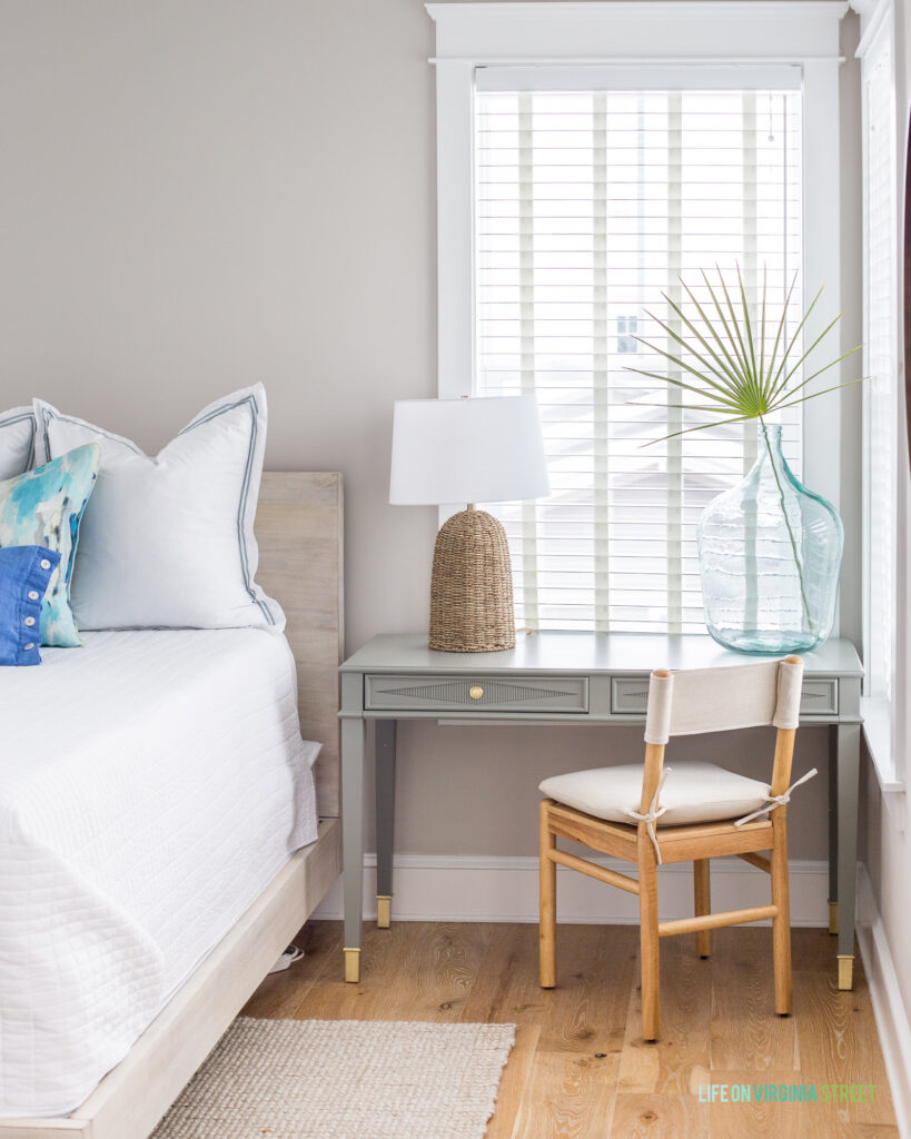 Hola Beaches 30a vacation rental bedroom with a gray desk, light wood bed, white bedding, a seagrass lamp and a wood chair.