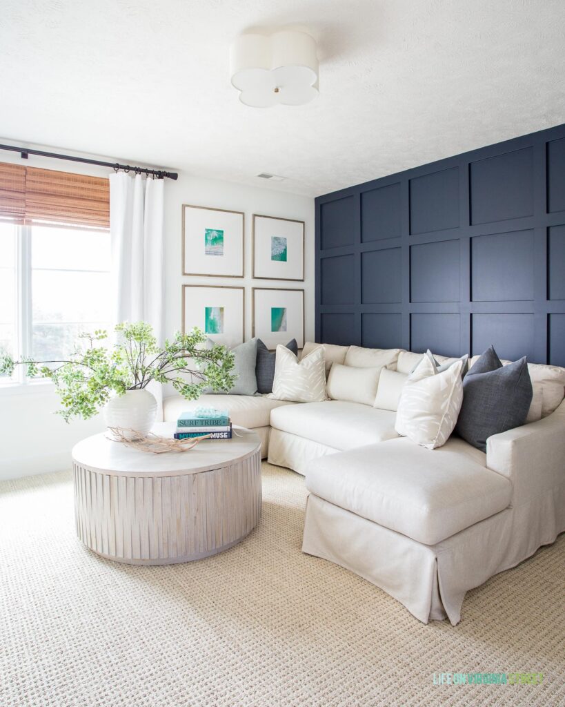 A light and bright living room with Benjamin Moore Hale Navy grid wall, linen sectional, round wood coffee table, white linen drapes, and an oversized gallery wall.