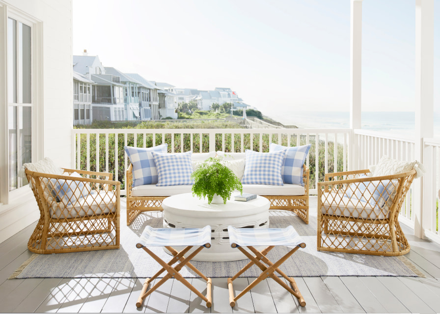 An outdoor porch inspired by the coastal grandmother aesthetic. Includes rattan furniture, gingham pillows, views of the ocean and light blue and white decor.