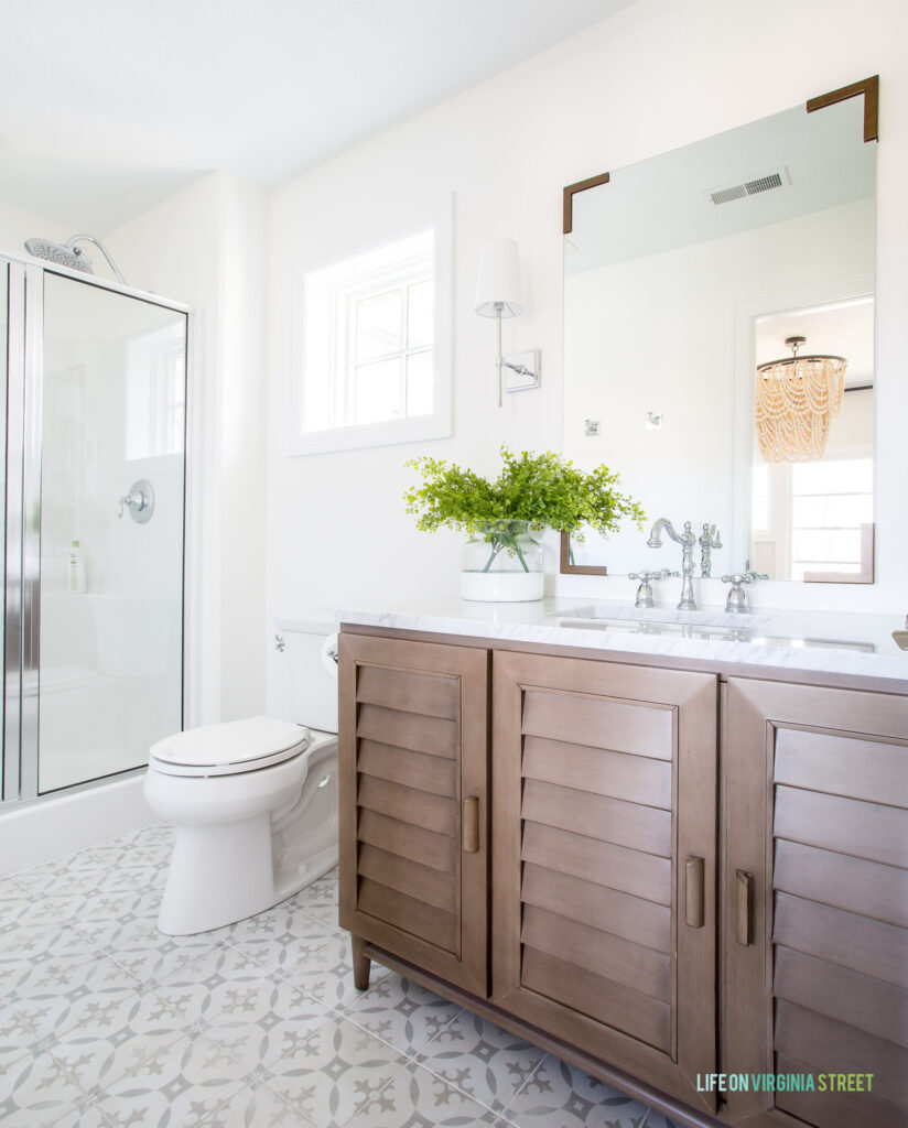 A louvered wood bathroom vanity with Carrara marble countertops and patterned tile floors.