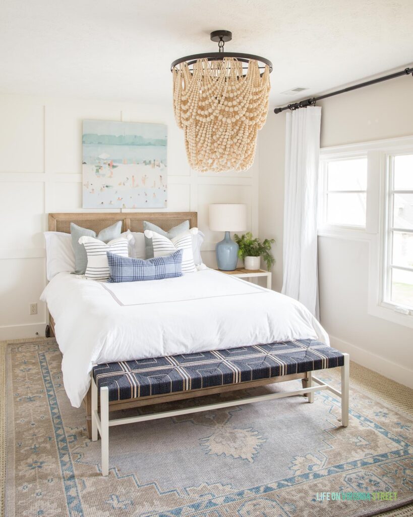 The best gray paint colors as shown in our coastal bedroom with walls painted Benjamin Moore Classic Gray. Includes a wood bead chandelier, coastal art, wood cane bed, white bedding, and a hand-knotted rug.