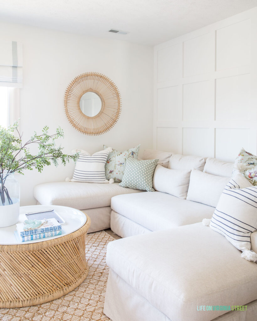 A round rattan mirror hung in a neutral TV room over a linen sectional.