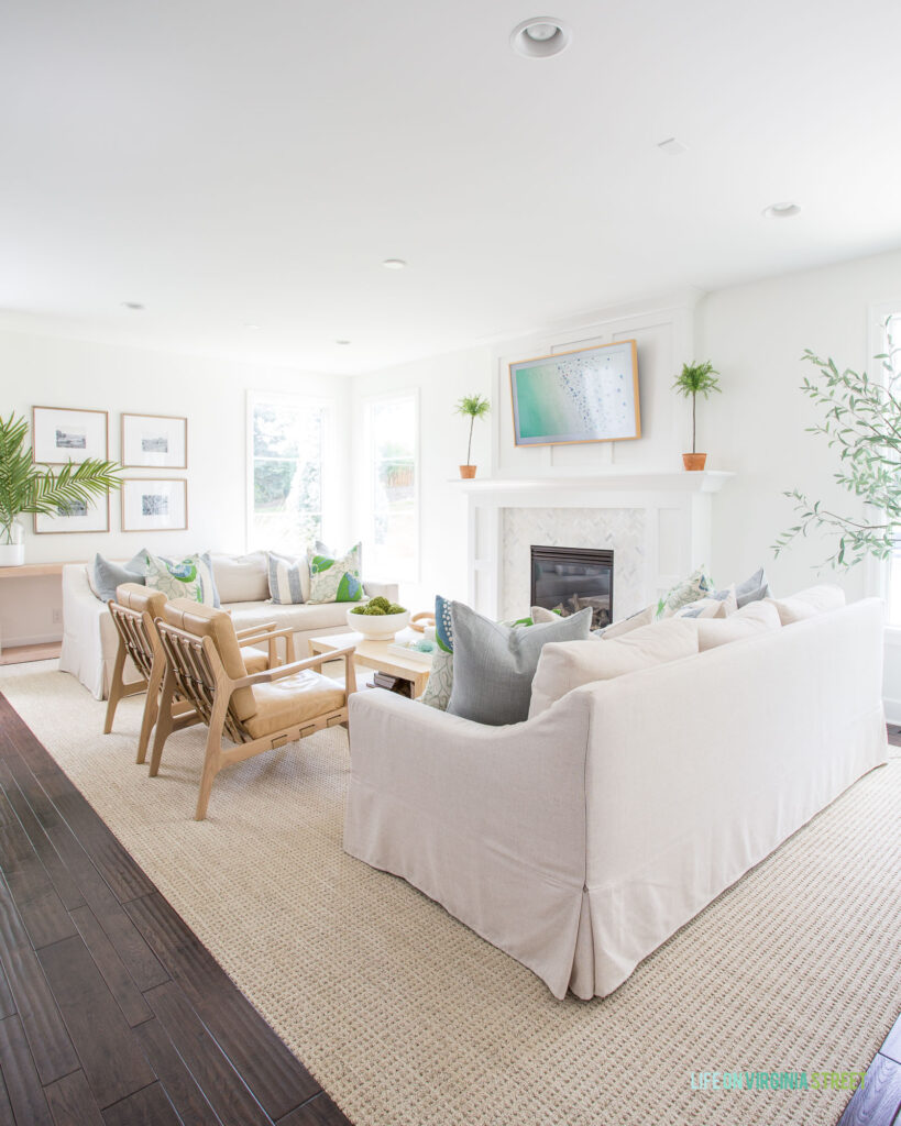 A 2022 summer home tour featuring a coastal inspired blue, white and neutral living room! Includes two linen sofas facing each other, light leather & wood chairs, a raffia coffee table, light wood gallery frames, and a Frame TV.