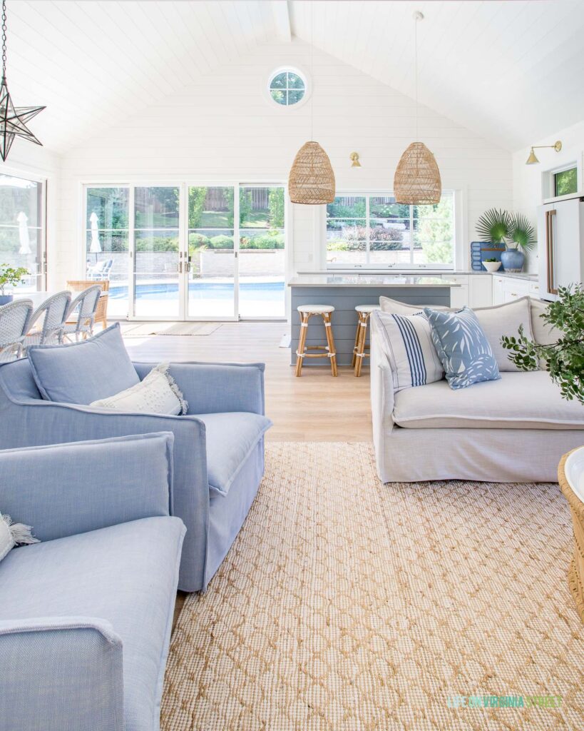 2022 summer home tour featuring a gorgeous pool house with white shiplap walls, a circle window in an a-frame roofline, basket pendant lights, performance furniture, and a jute rug.