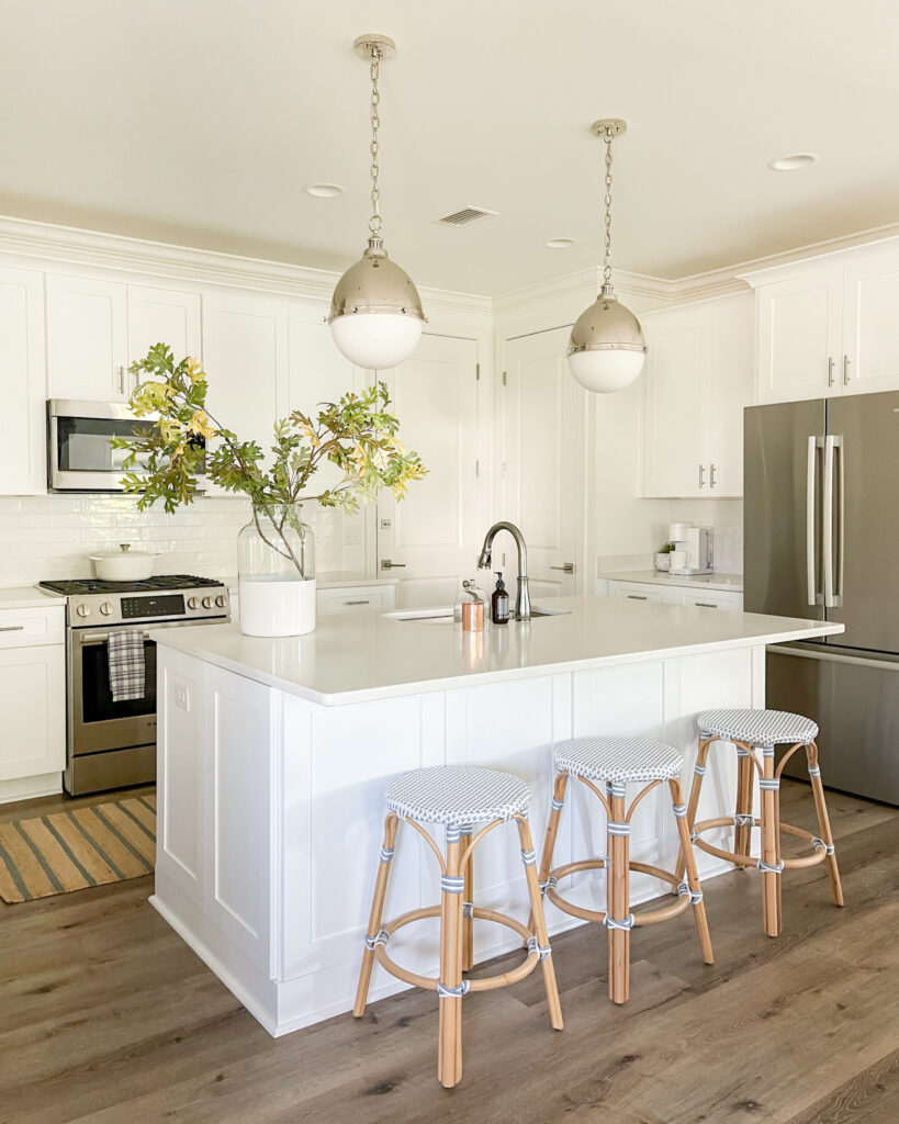 A white kitchen with a kitchen island where you'll find three backless counter stools and two globe pendant lights hanging above the island.