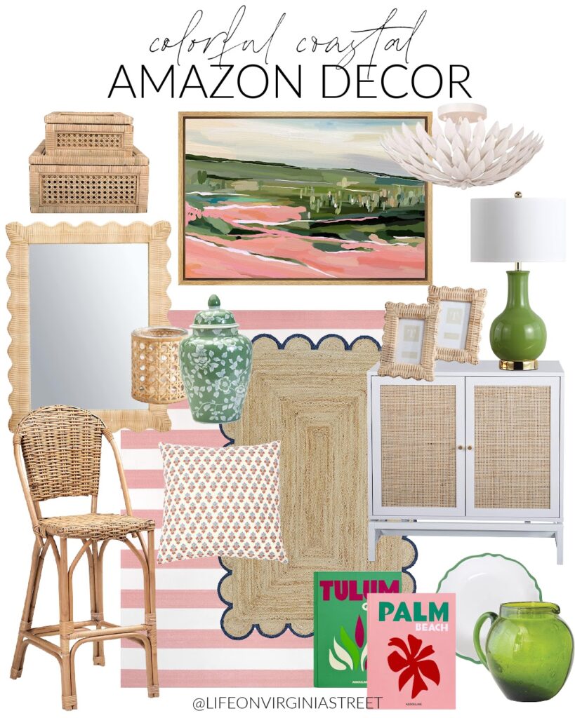 Colorful coastal Amazon decor inlcuding a pink and green landscape art, pink striped rug, colorful cofffee table books, a scalloped rattan mirror, a matte white light fixture, a rattan cabinet, woven counter stool, and a green lamp.