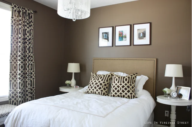 A guest bedroom painted Behr Mocha Latte, featuring trellis curtains and pillows, ivory table lamps, a linen headboard, and white chandelier.