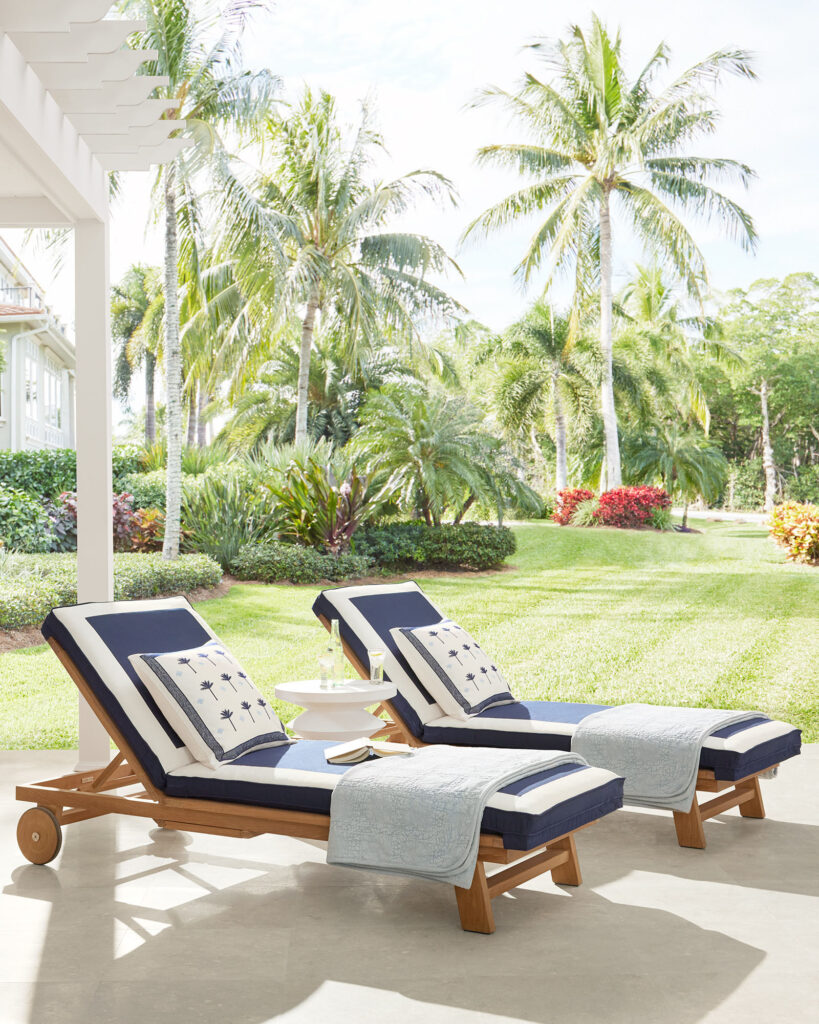 Tropical pool lounge chairs with a teak frame and white and navy blue border cushion.