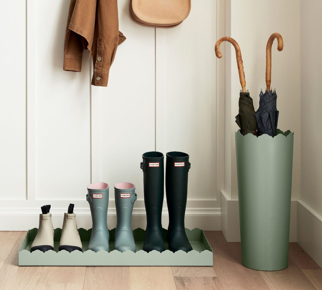 A sage green Scalloped Boot Tray & Umbrella Stand in a small entryway space with board and batten walls.