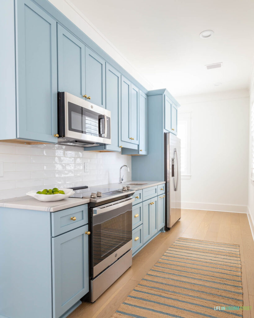 A Florida carriage house kitchen with Aero Blue cabinets, white oak hardwood floors, a striped jute rug, and a white bowl filled with limes.