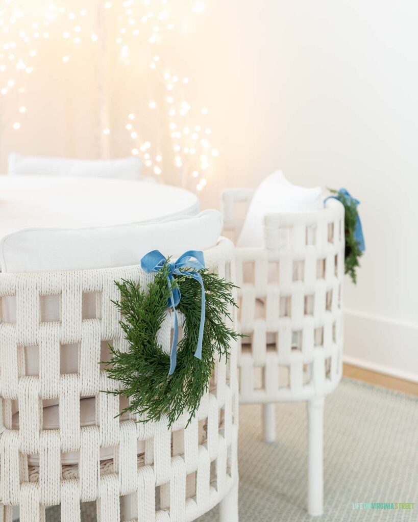 White dining chairs with a mini wreath and light blue velvet bow tied on the back.