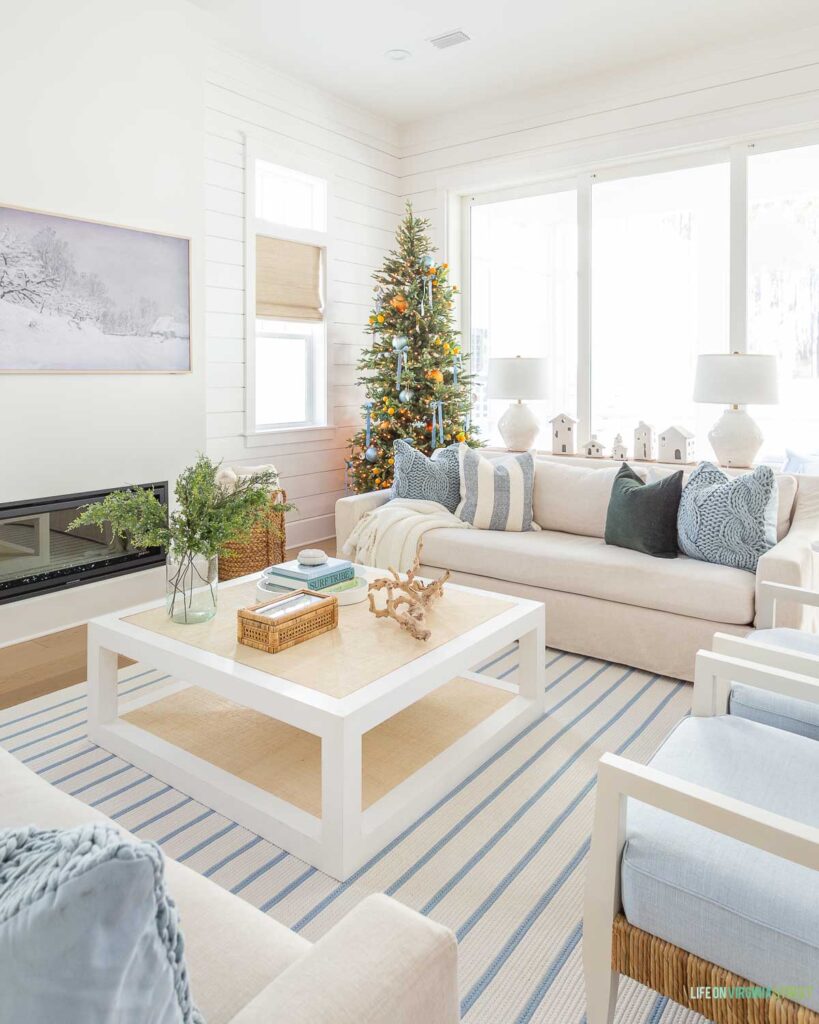 A coastal Christmas home tour showing a beautiful blue and white living room with orange Christmas accents! Includes a blue and white striped rug, Serena & Lily Mercer coffee table, slipcovered Pottery Barn sofas, a slim 9' Christmas tree and blue and green accents.