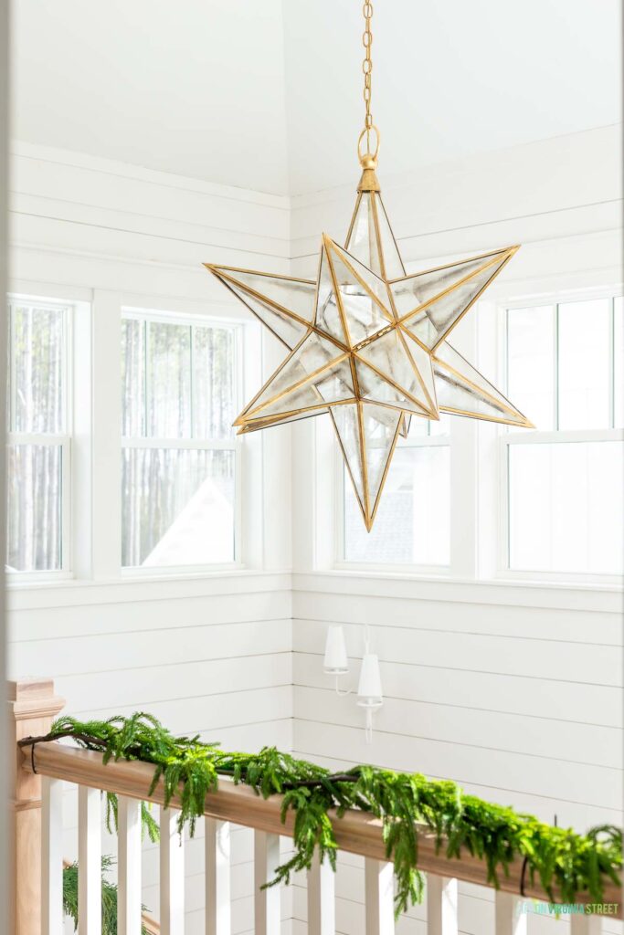 Visual Comfort XL Moravian Star Chandelier hanging in a coastal home entryway with white shiplap walls and garland on the staircase.