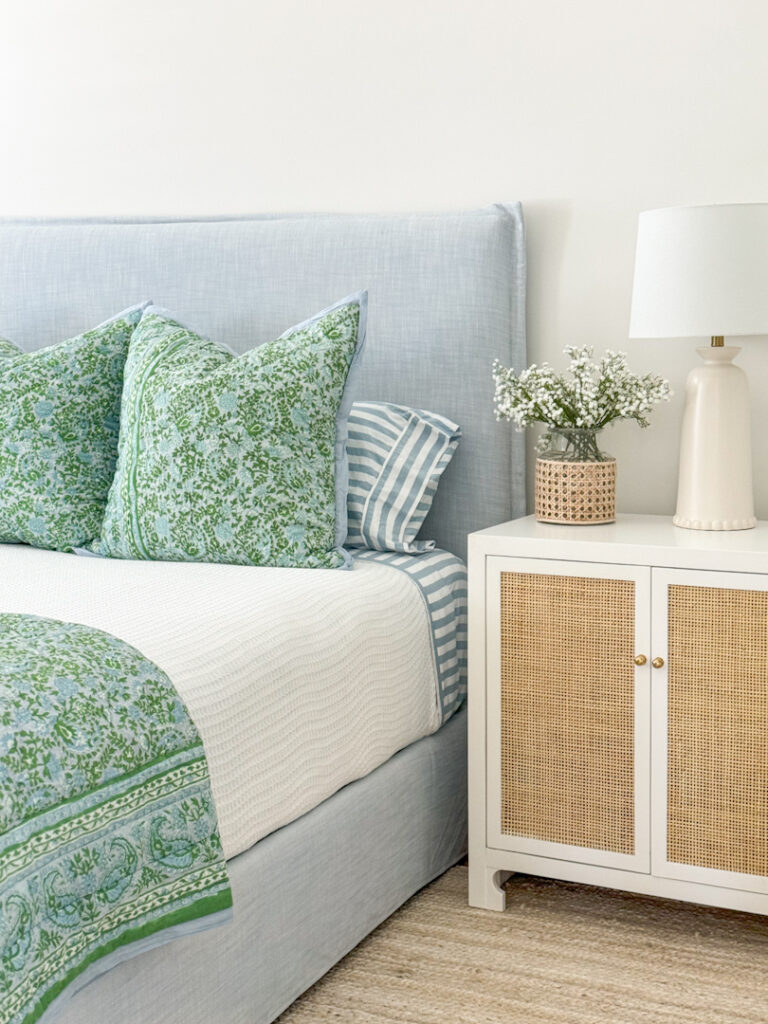 Simple bedroom updates to freshen up your spaces! This room includes a blue linen bed from Serena & Lily, white waffle knit blanket, a blue and green quilt, blue and white striped sheets, rattan nightstands, faux baby's breath in a cane wrapped vase, and a jute rug.
