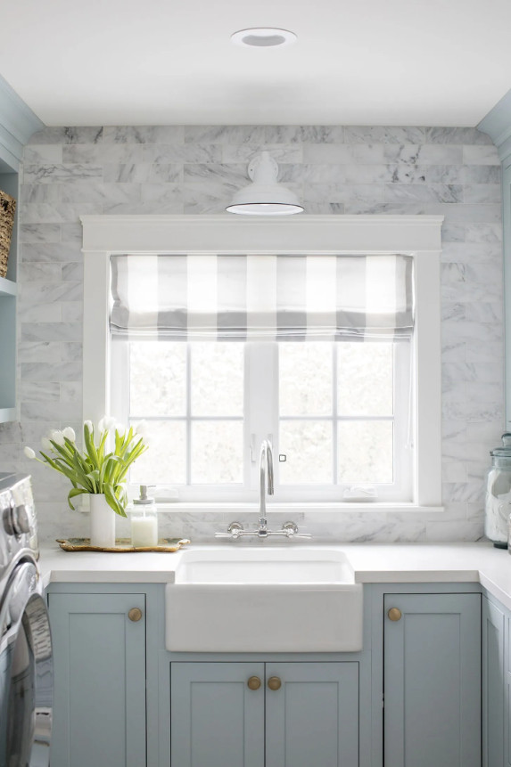 Benjamin Moore Smoke, one of the best blue gray paint colors, looks beautiful on these laundry room cabinets! Paired with Carrara marble subway tiles and coastal accents, the color really shines in this space.